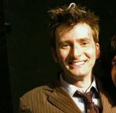 a man and woman posing for a photo in front of a dark background with one smiling at the camera