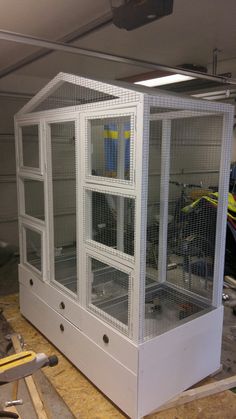 a large white bird cage sitting on top of a hard wood floor in a garage