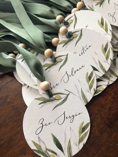 several tags with green leaves on them sitting on top of a wooden table next to ribbons