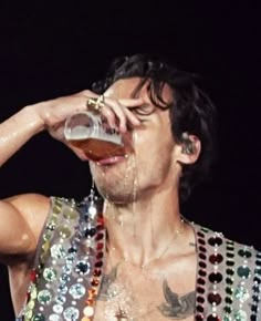 a man with no shirt drinking from a beer glass while wearing sequins on his vest