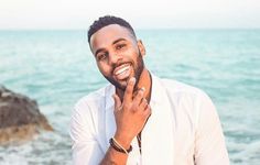 a man standing next to the ocean with his hand on his face and looking at the camera