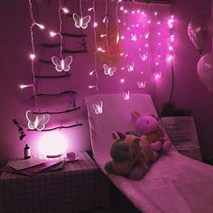 two stuffed animals sitting on top of a bed in a room with pink lights hanging from the ceiling