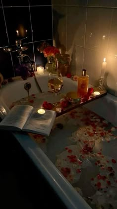 a bathtub filled with candles and rose petals next to a book on the floor