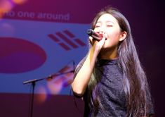 a woman singing into a microphone while standing in front of a stage with an advertisement behind her