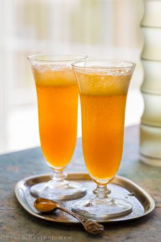 two glasses of orange juice sitting on top of a metal tray next to each other