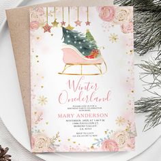 a pink and gold christmas card with a sleigh on it next to pine cones