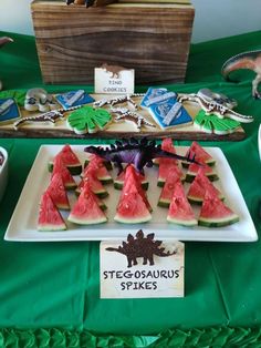 watermelon slices are arranged on a white plate and green tablecloth with dinosaur magnets