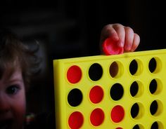 a child's hand holding a red and black object in front of a yellow board game