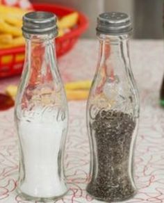 two glass bottles filled with salt and pepper sitting on a table next to french fries