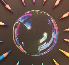 colored pencils are arranged in the shape of a ball on a black surface with an image of a person's face