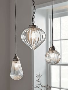 three clear glass pendant lights hanging from a ceiling in a room with white walls and windows