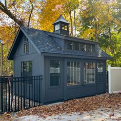 a small blue shed with a clock tower on the top and a black fence around it