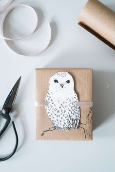 an owl is sitting on top of a piece of cardboard next to scissors and tape