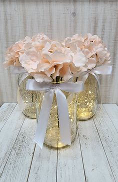 two mason jars filled with pink flowers on top of a white wooden table next to a wall