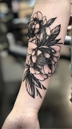 a black and white flower tattoo on the left arm, with leaves around it's center