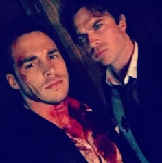 two men are posing for a photo with blood on their shirts and ties, one is wearing a black blazer