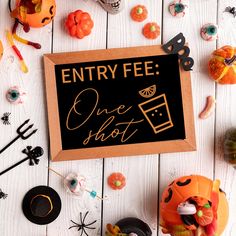 a sign that says entry fee one shot surrounded by halloween decorations and candies on a white wooden surface