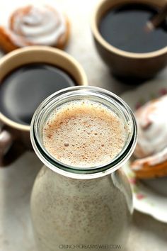 two cups of coffee sit next to each other on a table with pastries in the background