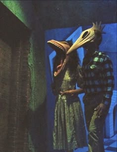 two people standing next to each other in front of a blue wall with an animal mask on it's head