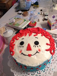 a birthday cake decorated with a clown face on top of a doily covered table