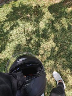 a person with their feet up in the air next to a motorcycle helmet on grass