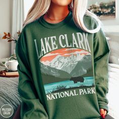 Show off your love of Alaska and one of our nation's most remote national parks with our Lake Clark National Park Sweatshirt! This comfy crewneck is all about embracing the great outdoors, featuring a custom vintage design that showcases the grandeur of the Alaskan Wilderness, the iconic Brown Bear, and the beautiful vistas across Lake Clark! The Gildan 18000 50/50 blend fabric has that comfy, lived-in feel, that's like a hug every time you put it on! Now you can take a bit of Lake Clark with yo National Park Shirts, National Park Sweatshirt, California Sweatshirt, National Park Gifts, National Park Shirt, Beautiful Parks, Great Smoky Mountains National Park, Beautiful Park, Smoky Mountain National Park