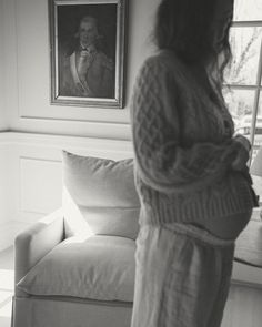 a woman standing in front of a couch with a painting on the wall behind her