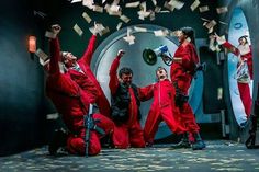 a group of people in red jumpsuits on stage with money falling from the ceiling