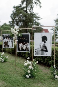 some pictures hanging on poles in the grass with flowers and greenery next to them