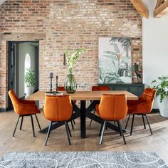 a dining room table with orange chairs in front of a brick wall and potted plants