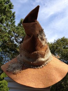 a large brown hat sitting on top of a white pillar in front of some trees