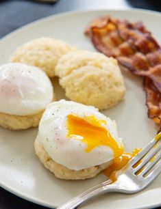 eggs, biscuits and bacon are on a plate with a fork next to the plate