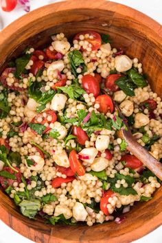 a wooden bowl filled with couscouse and vegetables on top of a table