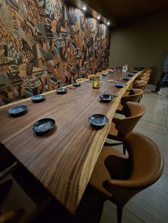 a long wooden table with plates on it in front of a wall covered with art