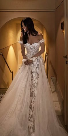 a woman in a wedding dress is standing on the stairs with her hands behind her back