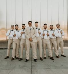 a group of men standing next to each other in front of a metal wall with ties on