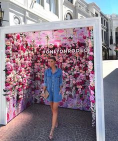 a woman standing in front of a flower covered wall with pink flowers on the side