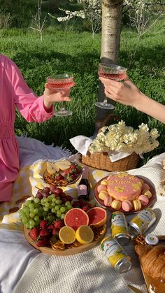 two women sitting at a picnic table holding wine glasses and plates with food on them