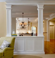 a living room filled with furniture and a chandelier hanging from the ceiling next to a kitchen