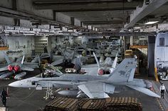 several fighter jets are on display in an aircraft hanger with people looking at them