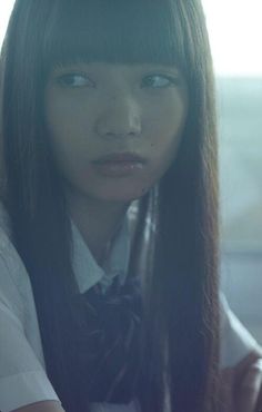 a woman with long black hair wearing a white shirt and bow tie looking at the camera