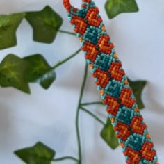 an orange and blue beaded bracelet sitting on top of a green leafy plant