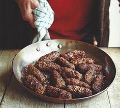 a person holding a cloth over a pan filled with meatballs on top of a wooden table