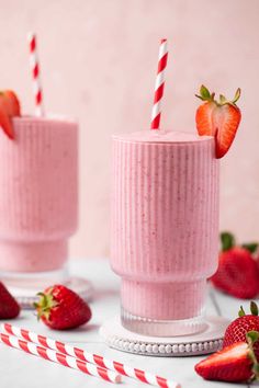 two smoothie cups with strawberries on the side and candy canes next to them