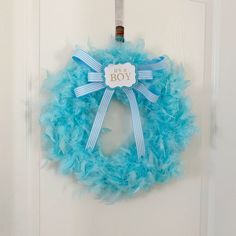 a baby boy wreath hanging on the front door with blue feathers and a name tag