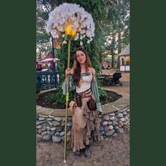 a woman dressed up as a pirate holding a large flower in her hand and standing next to a giant dandelion