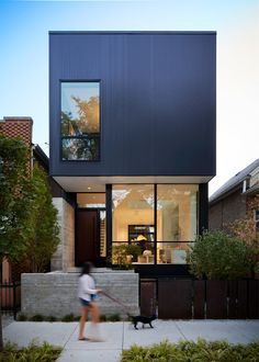 a woman walking her dog in front of a modern house