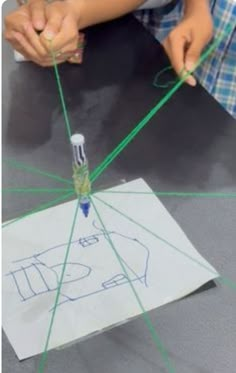 two children are working on an object with green string and glue in front of them