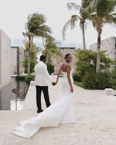 Elegant bride in fitted white gown with dramatic train holding groom's hand at tropical luxury resort with swaying palm trees and stone architecture Resort Wedding Dress, Travel Wedding Theme Decoration, Wedding Locations Beach, Minimalist Wedding Design, Destination Wedding Attire, Tropical Wedding Photography, Outdoor Ceremony Ideas, Luxury Beach Wedding, Tropical Wedding Venue