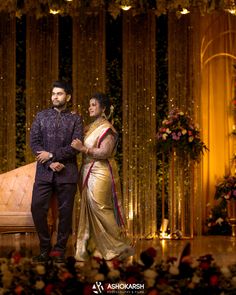 a man and woman standing next to each other in front of a stage decorated with flowers